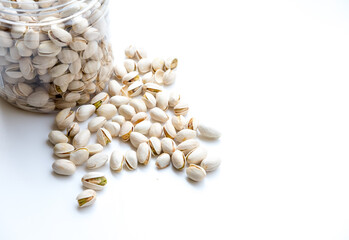 An open container of pistachios tipped over, spilling the nuts onto a white surface. The pistachios, in their partially open shells, showcase the vibrant green nuts inside, highlighting texture and co