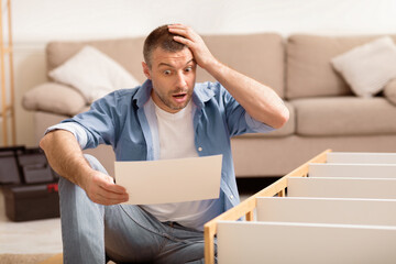 Shocked Man Assembling Furniture Scratching Head Reading Difficult Manual Inctruction Furnishing House Sitting Indoor. Selective Focus