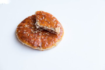 Round, golden-brown Chinese Sweet Pie (Laobing), partially broken to reveal the filling, sprinkled with sesame seeds on a white surface. A simple and sweet pastry