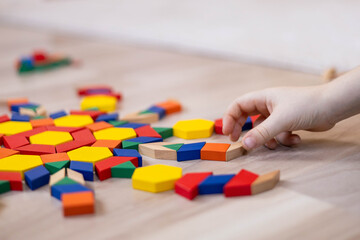 A child plays with geometric shapes and makes a colorful circular mandala pattern from a mosaic.