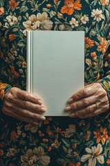 Elderly Hands Holding a Blank White Book Against a Floral Background