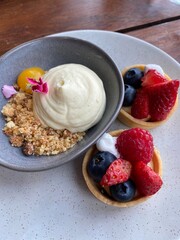 Berry fruit tarts and mascarpone cheesecake served on the white plate on the wooden table 