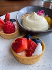 Berry fruit tarts and mascarpone cheesecake served on the white plate on the wooden table 