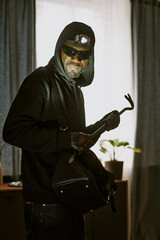 Vertical portrait of African American thief with headlamp and crowbar in hands smiling while...