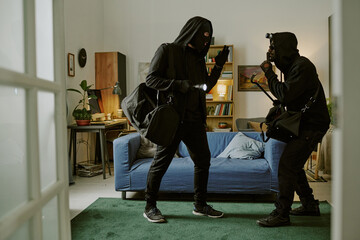 Crime partners in total black clothes with big bags and instruments in hands keeping silent in...