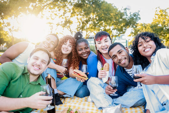Group of diverse people having fun at garden party. Happy friends eat food and drink wine in picnic together