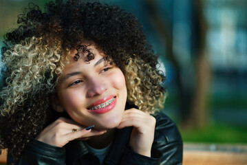 Beautiful Latina woman with braces and afro hair, enjoying and smiling with confidence, on a sunny day outdoors. Lots of joy and positivity