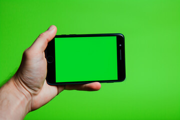  Close-up view of hand holding smartphone with green screen against a green background
