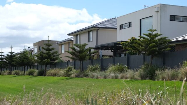 A row of modern Australian suburban residential houses lined up behind a boundary fence in a peaceful neighborhood, representing concepts of housing, real estate, homeownership, property investment.