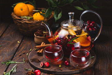 Tea with berries, citrus fruits and spices in a glass teapot and mugs