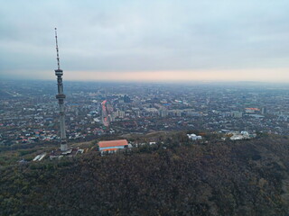 Naklejka premium Koktobe TV tower on a hill at sunset, against the background of the city. Cloud cover. Autumn. The view from the drone.