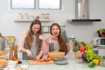 POV of Caucasian mother and daughter greeting to audience showing cooking homemade salad streaming online in the kitchen. girl enjoy family activity.