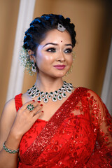 Portrait of beautiful young Indian woman wearing a traditional red saree adorned with delicate jewellery posing fashionably in studio lighting