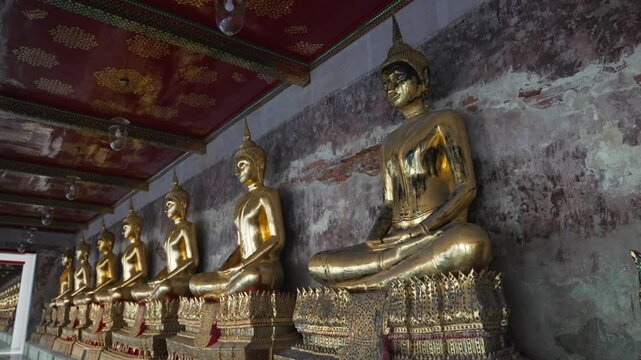 A row of many statues of a gold Buddha sitting in a meditative pose in the courtyard of a Buddhist temple Wat Pho. The most visited tourist place in Bangkok, Thailand