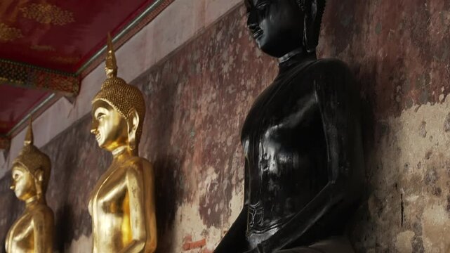 Close up of a black Buddha sitting among the golden statues in a meditative pose in the courtyard of a Buddhist temple Wat Pho. The most visited tourist place in Bangkok, Thailand