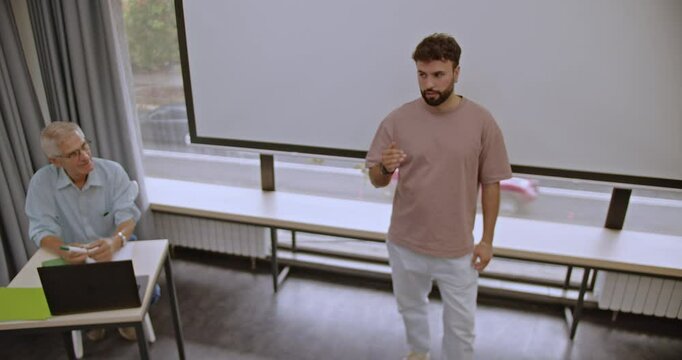 A nervous male college student gives a presentation in front of his professor at school.