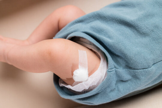 Newborn baby boy legs with a band aid patch after taking a vaccine