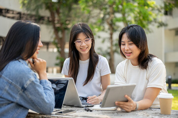 Group of Asian female college students is working on a project together at a table in a college park