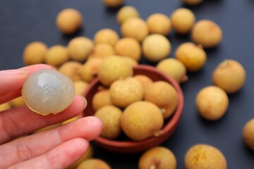 Woman's hand holding longan fruit or Dimocarpus longan, on a dark background, with close view.
