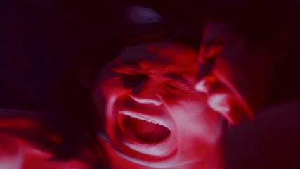 Emotional man pressing his head against distorting mirror, screaming in anguish or anger, creating surreal and unsettling atmosphere in dark studio with red illumination