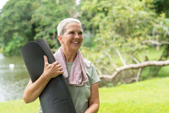 Happy and Healthy Elderly Woman Enjoying Outdoor Exercise with Yoga Mat in a Lush Green Park