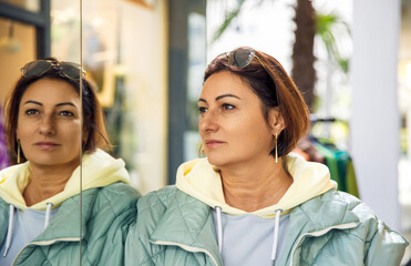 Woman in casual streetwear reflecting on her image in a shop window