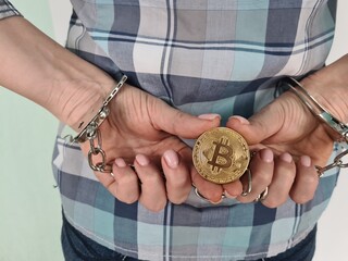 Person in handcuffs holding a Bitcoin symbolizing the intersection of crime and cryptocurrency in modern finance