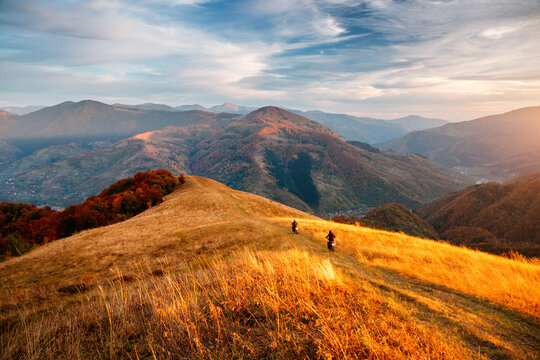 Two motorcyclists ride down a mountainside in the evening sun. Carpathian mountains, Ukraine.