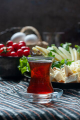 Beautiful breakfast scene with of  piping hot Turkish tea served in a traditional glass on a handwoven table cloth with a rich cheese platter, tomato and eggs in the background