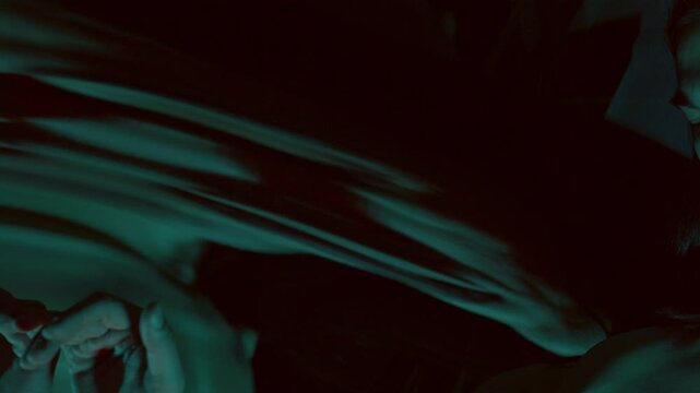 Contemplative man holding his hand on distorting mirror and looking around in dark studio with red and blue lighting