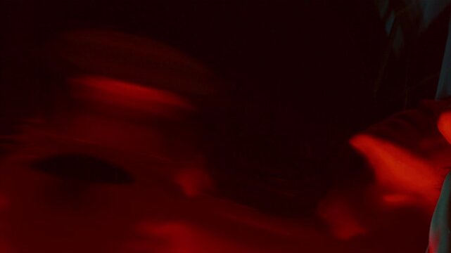 Amazed man staring incredulously at his warped reflection in distorting mirror in dark room with red illumination