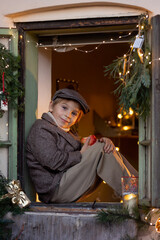 Beautiful blond child, boy, sitting on a christmas decorated window, drinking milk and eating apple, waiting for Santa Claus, Christmas concept