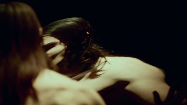 Amazed shirtless man with long hair looking around at surreal, distorted reflections of himself in dark room with mirrored wall