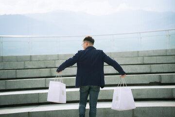 Serious stylish young man with sunglasses walking in urban street and enjoying Black Friday shopping in trendy stores in city