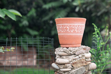 Rustic Clay Pot on the block of stones in Nature near the metal net fence - Earthy Outdoor Setting