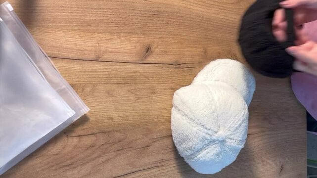 A woman is taking white and black fur caps out of the packaging. She is reviewing the purchase. Vertical video
