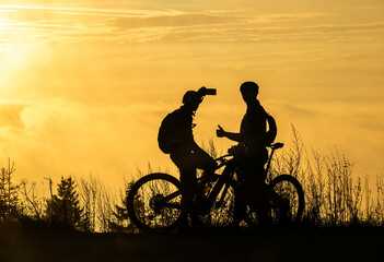 silhouette of two cyclists taking selfies on their mobile phones