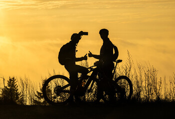 silhouette of two cyclists taking selfies on their mobile phones