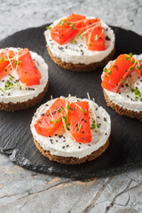 Sandwich, toast with smoked salmon, cream cheese, sesame and micro greens for healthy breakfast close-up on slate plate on the table. Vertical