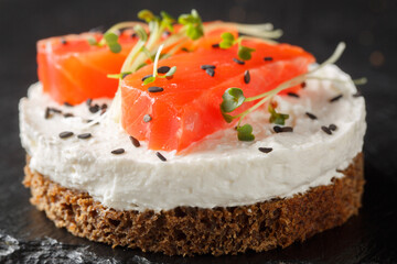 Smorrebrod traditional Danish sandwich with Black rye bread, salmon, cream cheese, sesame and micro greens for healthy breakfast close-up on slate plate on the table. Horizontal