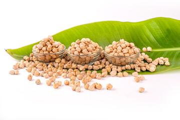 Dried chickpeas in white bowl on white. Spilled chickpeas.