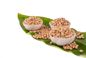 Dried chickpeas in white bowl on white. Spilled chickpeas.