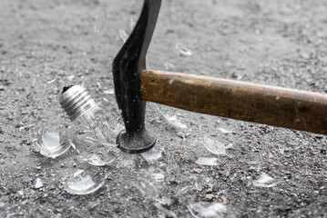 Hammer and broken bulb with spilled glass on ground, closeup photo, Incandescent bulb shattering with a hammer strike, fragments visible