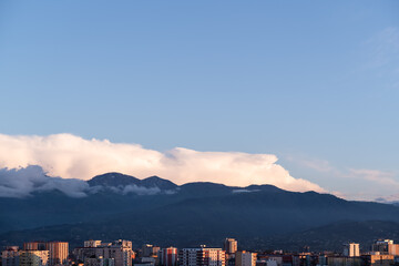 Cityscape of panel buildings in warm orange sunset light, framed by distant mountains and a clear blue sky, capturing the peaceful contrast of urban life against a natural backdrop