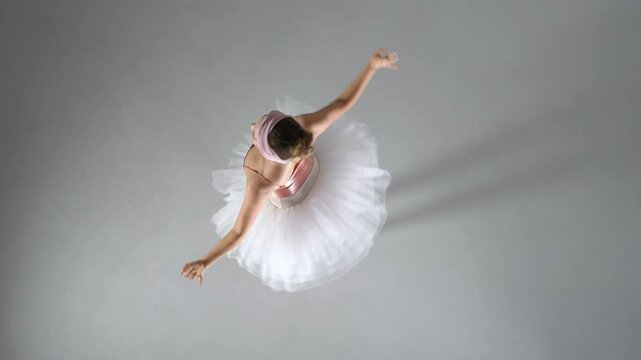 Ballerina in a pink tutu dance and perform dramatic choreographic elements on a white background, top view.