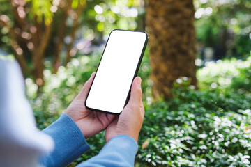 Mockup image of a woman holding mobile phone with blank white desktop screen in the outdoors
