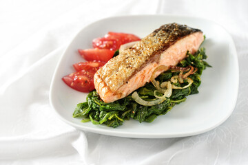 Roasted salmon fillet with skin with spinach vegetables, onions and tomatoes, healthy meal for low carb diet on a white plate and tablecloth, copy space