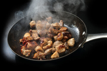 Diced pork is seared with tomato paste and a lot of steam in a cast iron frying pan, black...