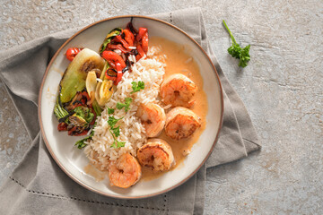 Fried prawns with crustacean sauce, rice and vegetables on a beige plate and napkin on a stone background, cooking in Asian style, top view from above copy space