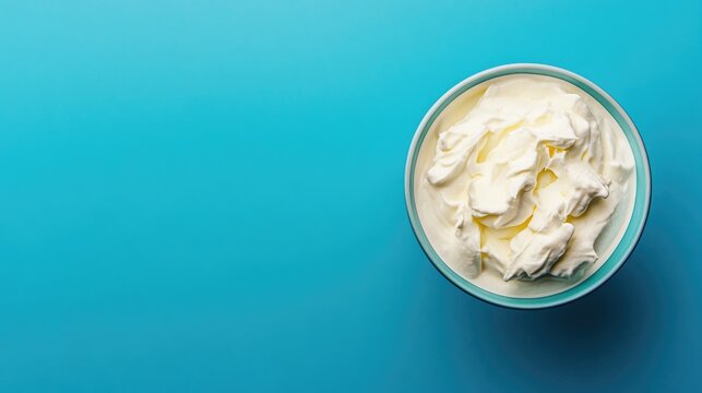 Top view of a bowl filled with white quark or cream against a blue background featuring ample copy space